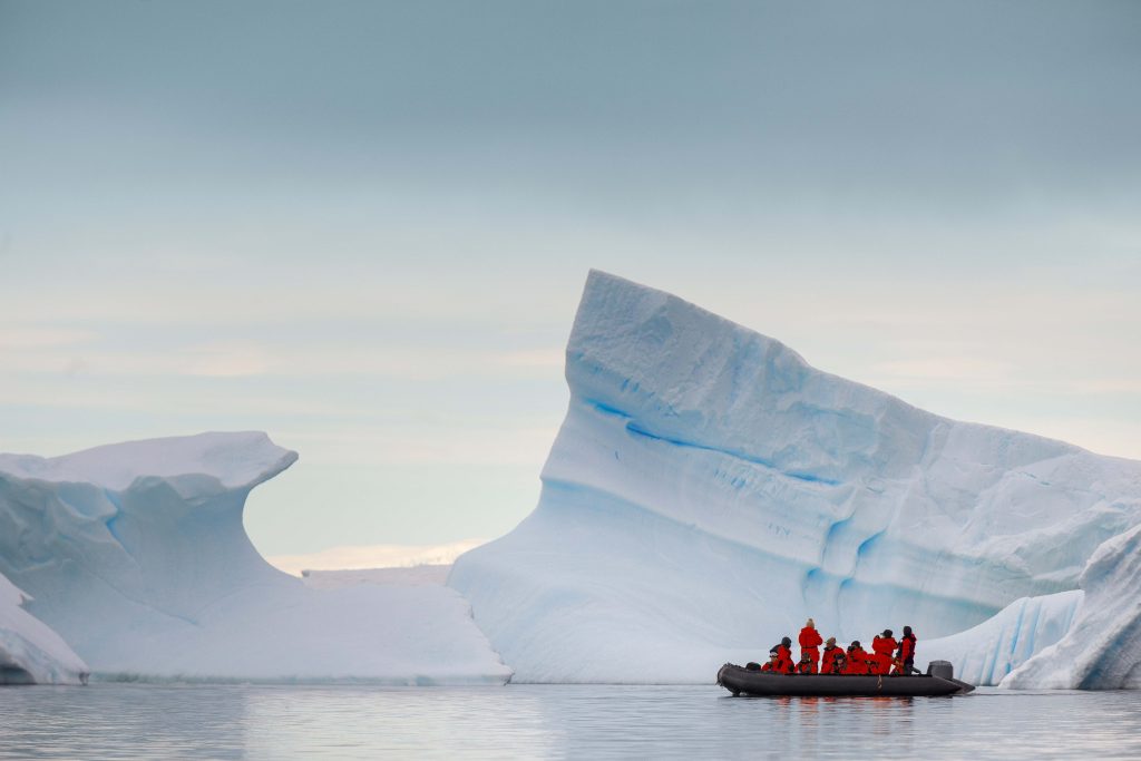 A small boat floats past Antarctic icebergs